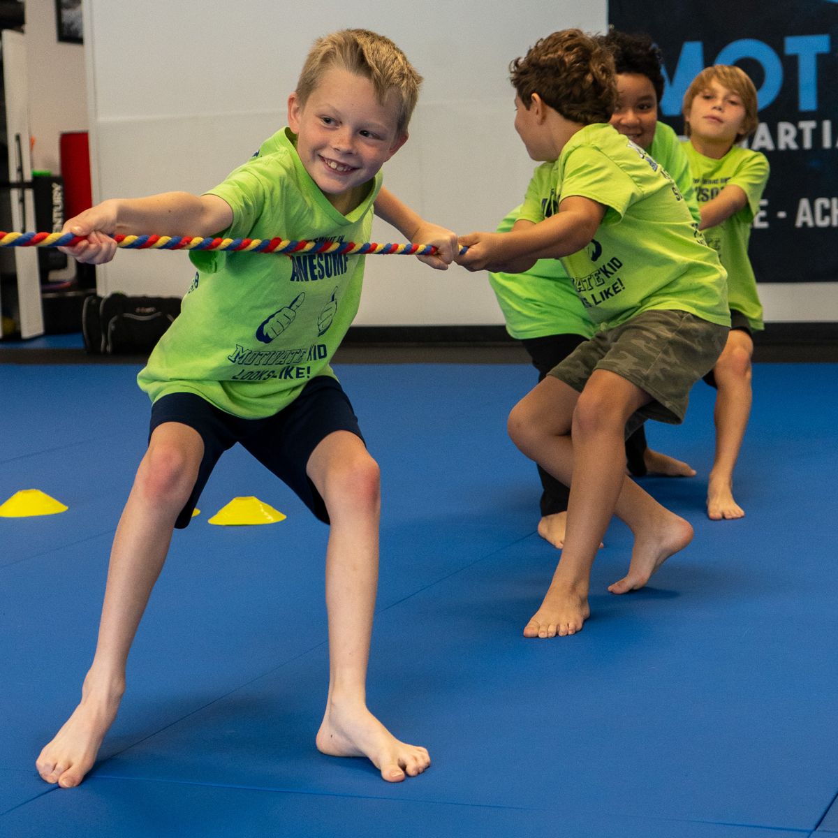Smiling campers in Motivate shirts playing tug of war on the mat