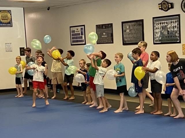 A long line of kids on the blue mats laughing as they keep balloons up in the air