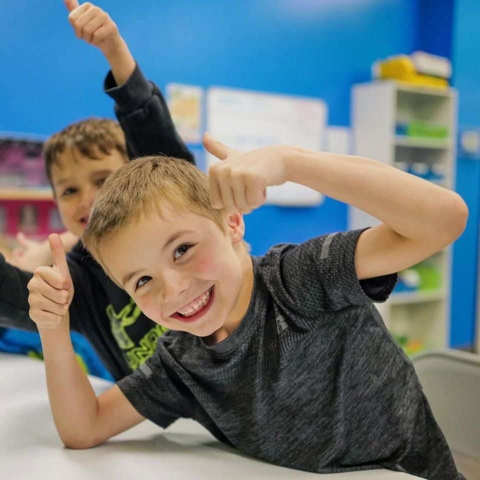Two smiling Motivate kids giving a thumbs-up at the table