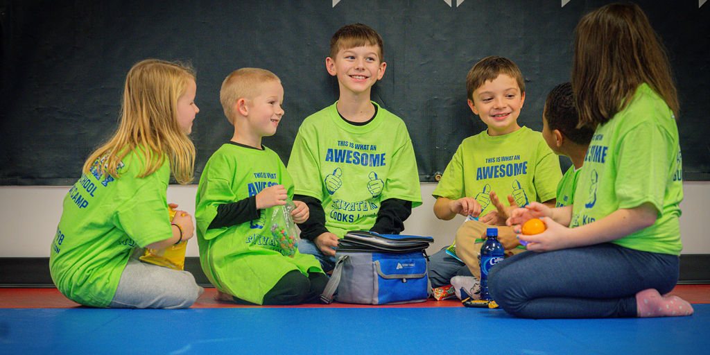 Six campers in lime Motivate shirts sitting in a circle on the mat with their lunch bag and snacks