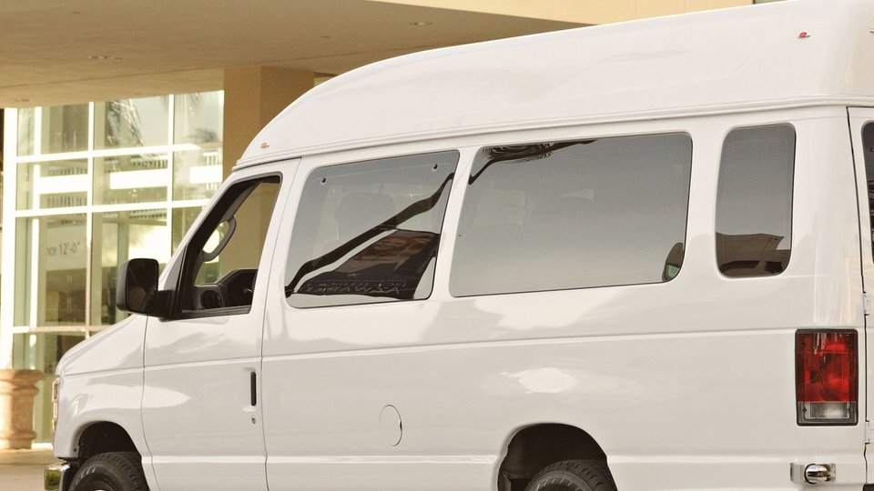 A white passenger shuttle van parked at a building entrance